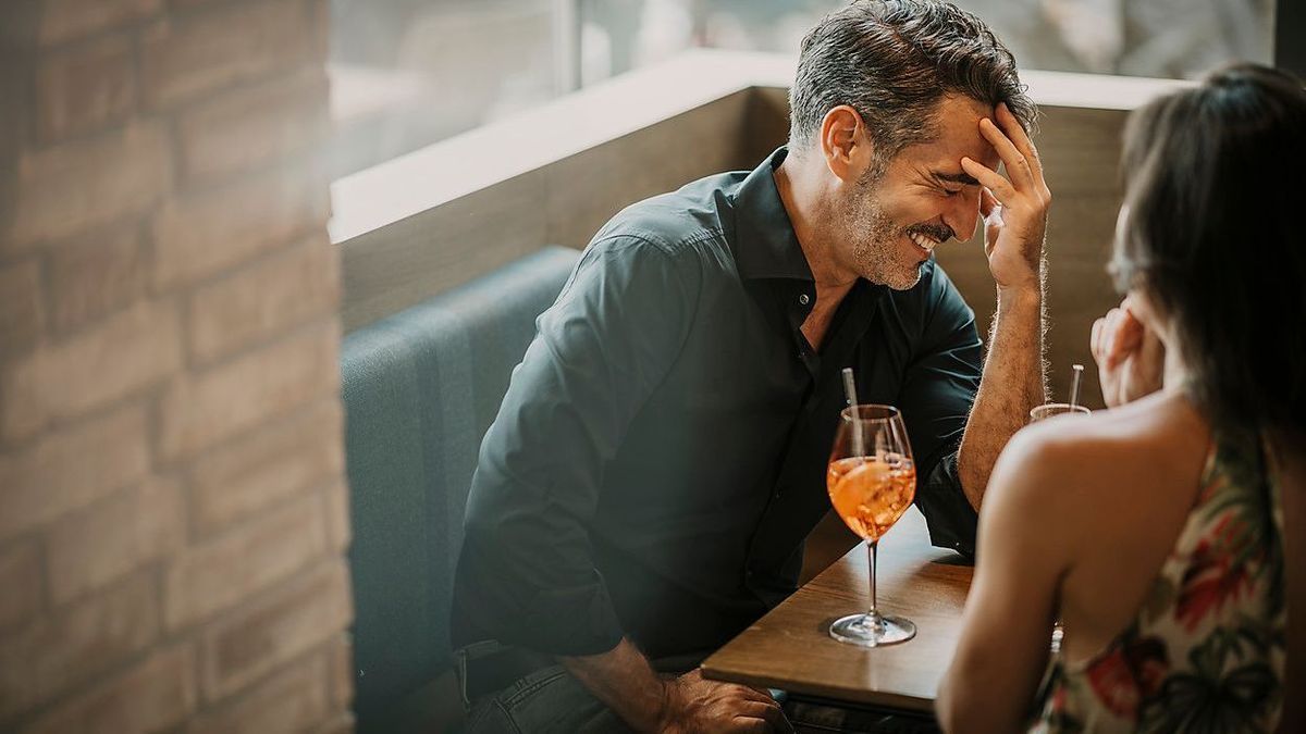 Happy man with drink sitting by girlfriend in restaurant