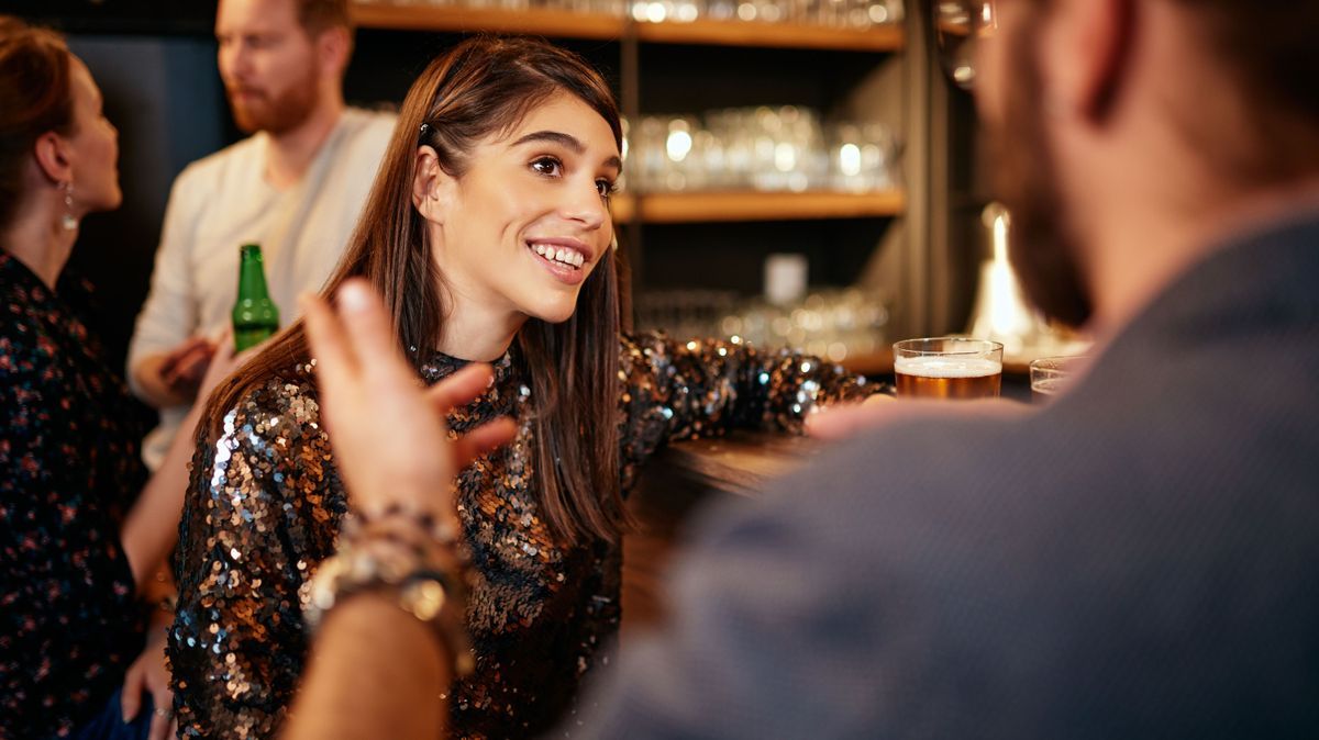 Rear view of handsome caucasian man leaning on bar counter, drinking beer and flirting with woman he just met. Pub interior.