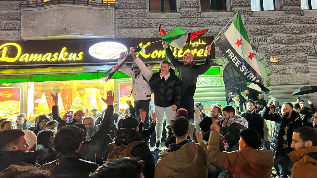 Berlin: Syrer versammeln sich im Bezirk Neukölln mit Flaggen vor der Bäckerei Damaskus und feiern den Vormarsch der Rebellen auf Damaskus.