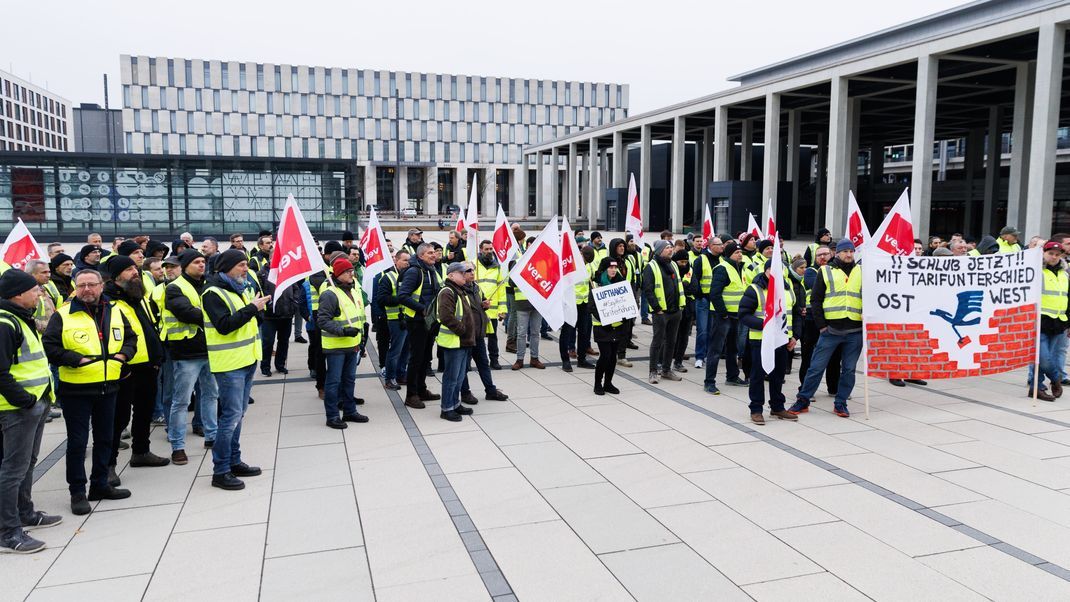 Mitarbeiter der Unternehmenssparte Lufthansa Technik demonstrieren mit einem Transparent und Fahnen vor der Abflughalle im Terminal 1 des Flughafens Berlin Brandenburg.