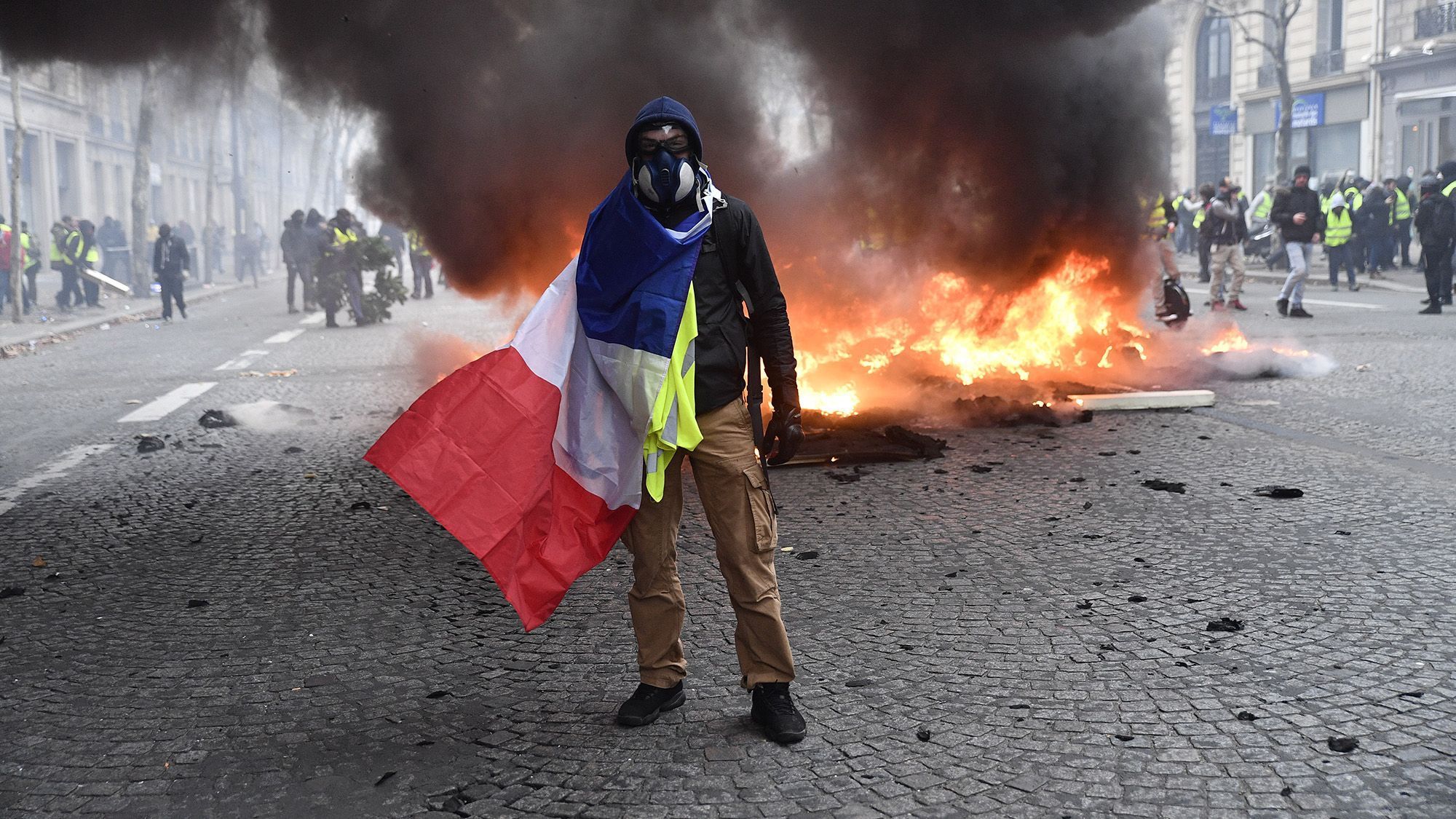 Ein Protestant der "Gelben Westen" steht im achten Arrondissement mit einer französischen Fahne vor einem brennenden Auto.