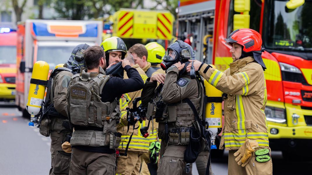 Polizeibeamte mit Gasmasken und Feuerwehrleute stehen vor einem Ratinger Hochhaus.