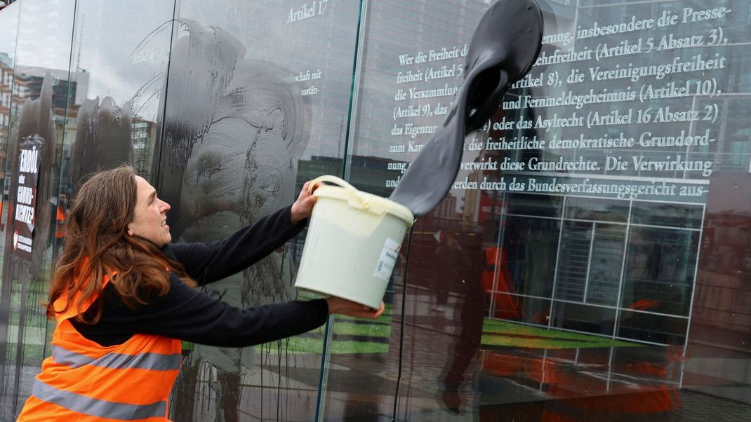 Eine Aktivistin der "Letzten Generation" klatscht schwarze Farbe auf das Denkmal.
