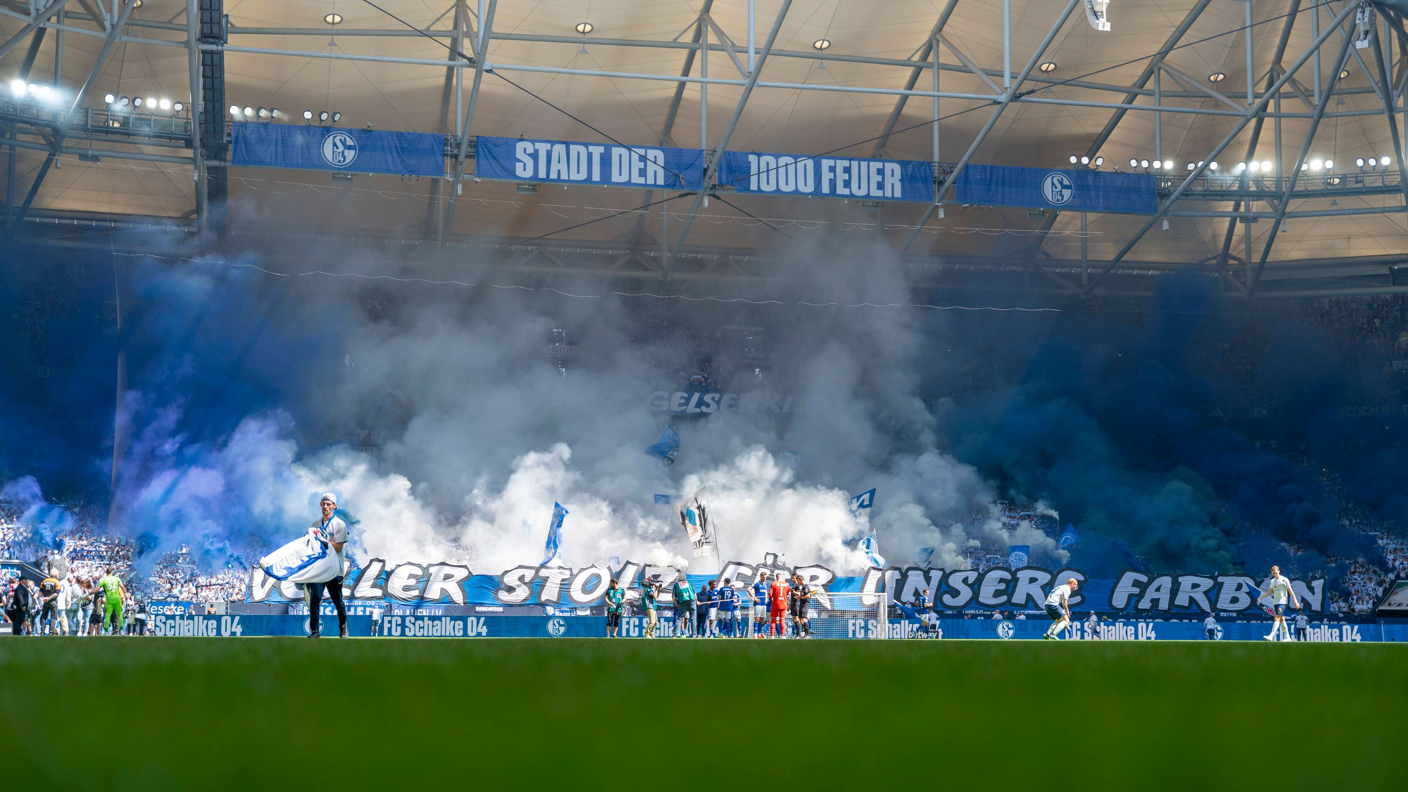 <strong>Schalke-Fans feiern Verein trotz bescheidener Saison</strong><br>Statt dem Aufstieg kann bei Schalke 04 im Heimspiel gegen Hansa Rostock nur der Nichtabstieg aus der 2. Liga gefeiert werden. Die Atmosphäre ist dennoch bundesligatauglicher als in einigen Stadien des Oberhauses. Samt blau-weißem Rauch präsentieren die Fans den Spruch: "Voller Stolz für unsere Farben".