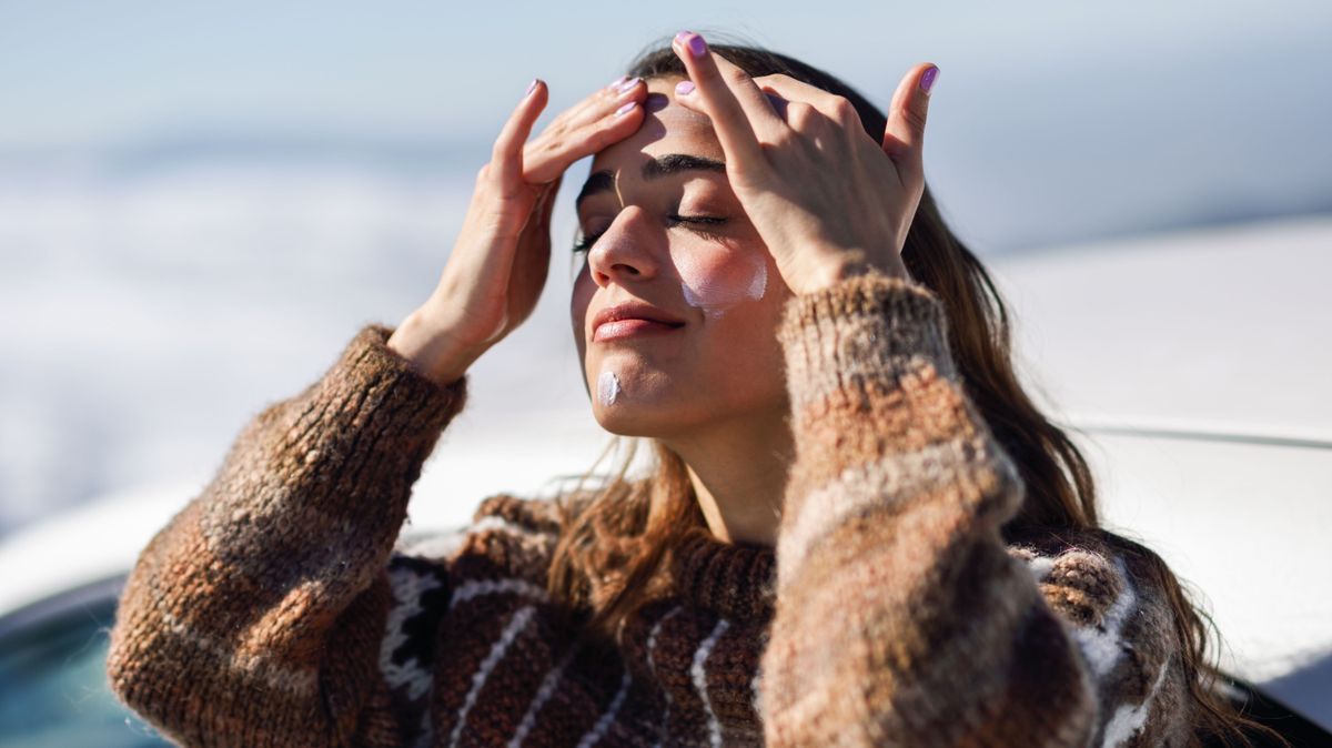 Young woman applying sunscreen on her face in snow landscape