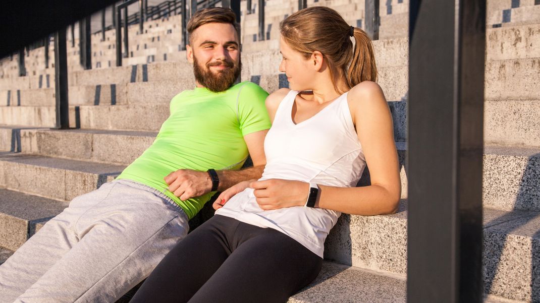 Young sporty couple are resting and check their fitness watch together. sport and technology concepts. || Modellfreigabe vorhanden