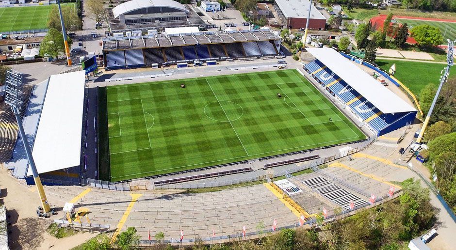 
                <strong>Jonathan-Heimes-Stadion am Böllenfalltor</strong><br>
                Der SV Darmstadt droht das beliebte Jonathan-Heimes-Stadion am Böllenfalltor als Heimspielstätte zu verlieren. Die DFL fordert, dass die Lilien die Gegengerade des Stadions überdachen lassen. Die Frist bis zur Fertigstellung: 31. Januar 2018. Sollte der Klub diese Umbaumaßnahme ablehnen, gibt es zwei Alternativen für den Erhalt der Liga-Lizenz. Entweder müssten die Darmstädter in ein Ausweichstadion umziehen oder ...
              