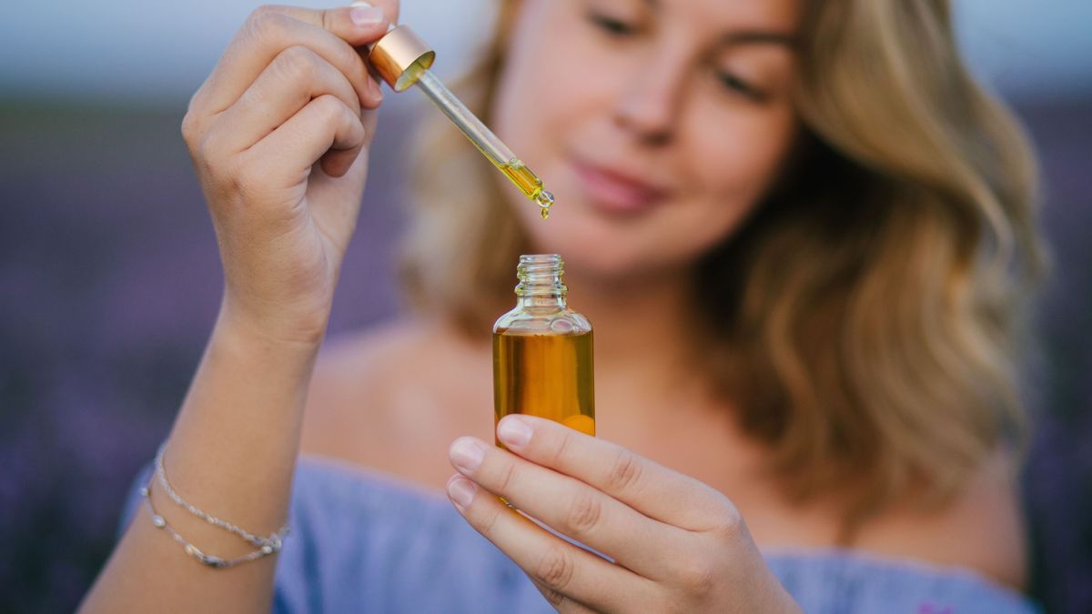 Woman holding bottle with natural essential oil in a lavender field.