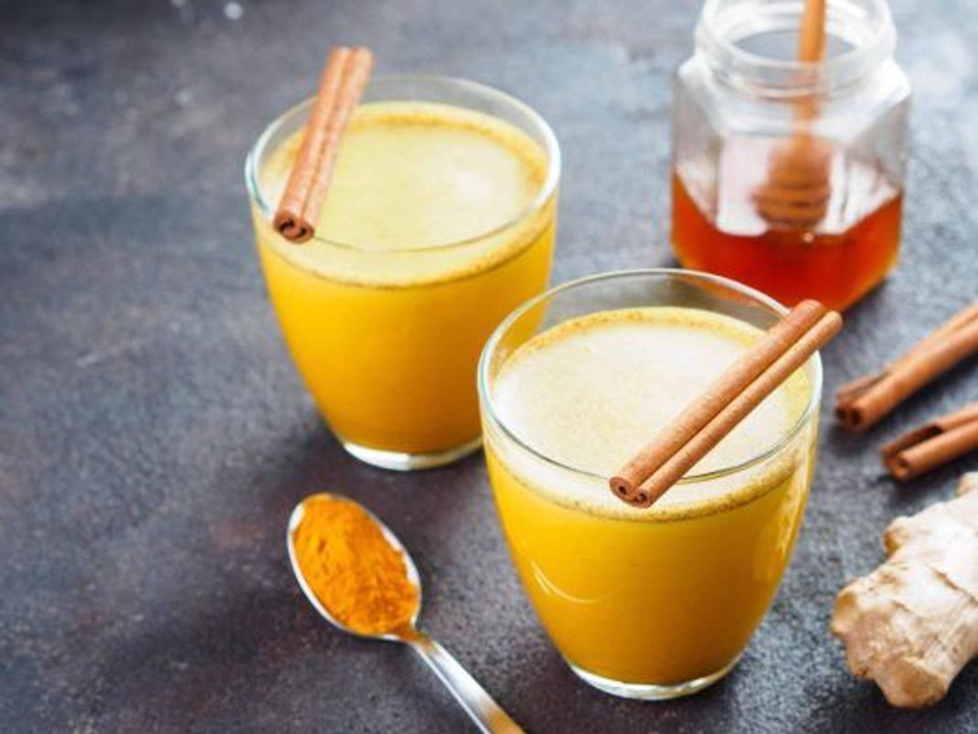 2 Gläser golden milk, dekoriert mit mit Honig, Ingwerwurzel, Zimtstangen und Kurkumapulver.
