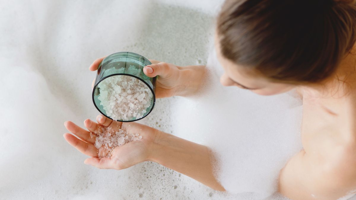 Top view of woman sitting in foam bath with sea bath salt in hands.