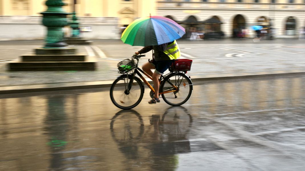 Ein Mann fährt bei Regen mit einem bunten Schirm Fahrrad