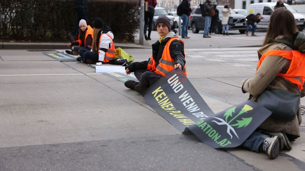 Klimaaktivist:innen sitzen mit einem Banner auf einer Straße. Im Dezember waren die Wohnungen einiger  Mitglieder durchsucht worden.