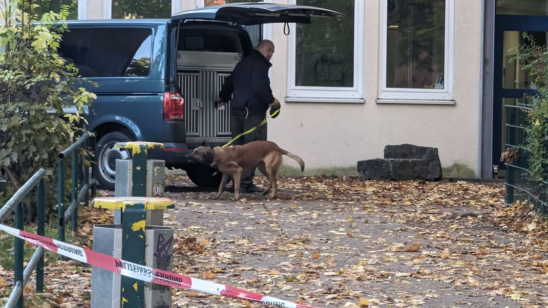 Ein Polizist steht mit einem Spürhund vor einem Schulgebäude in Erfurt.