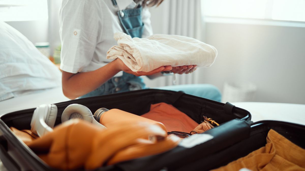 Holiday, packing and woman travel suitcase on a bedroom bed ready for vacation and adventure. Hands holding clothes for journey, trip or cruise with a suitcase, luggage and bag for traveling