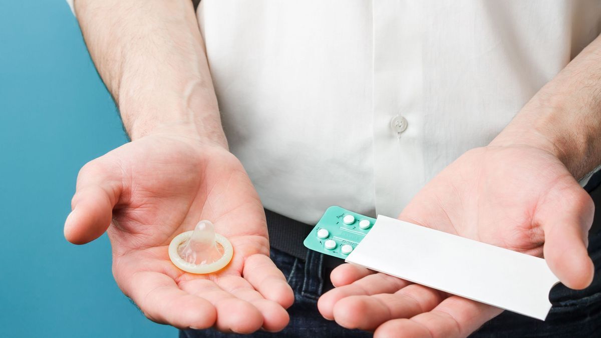 Ein Mann hält ein Kondom und Pillen in der Hand