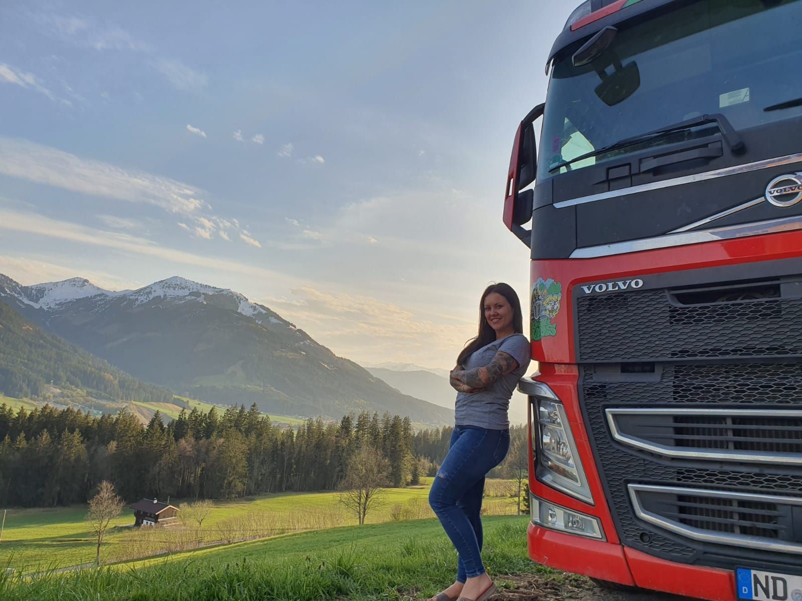 "Trucker Babe" Gina vor malerischer Bergkulisse mit ihrem roten Volvo 460.