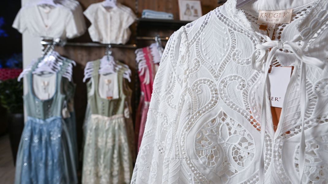 Blusen aus Spitze sind in einem Fachgeschäft in Esslingen ausgestellt.Im Hintergrund hängen Dirndl. 