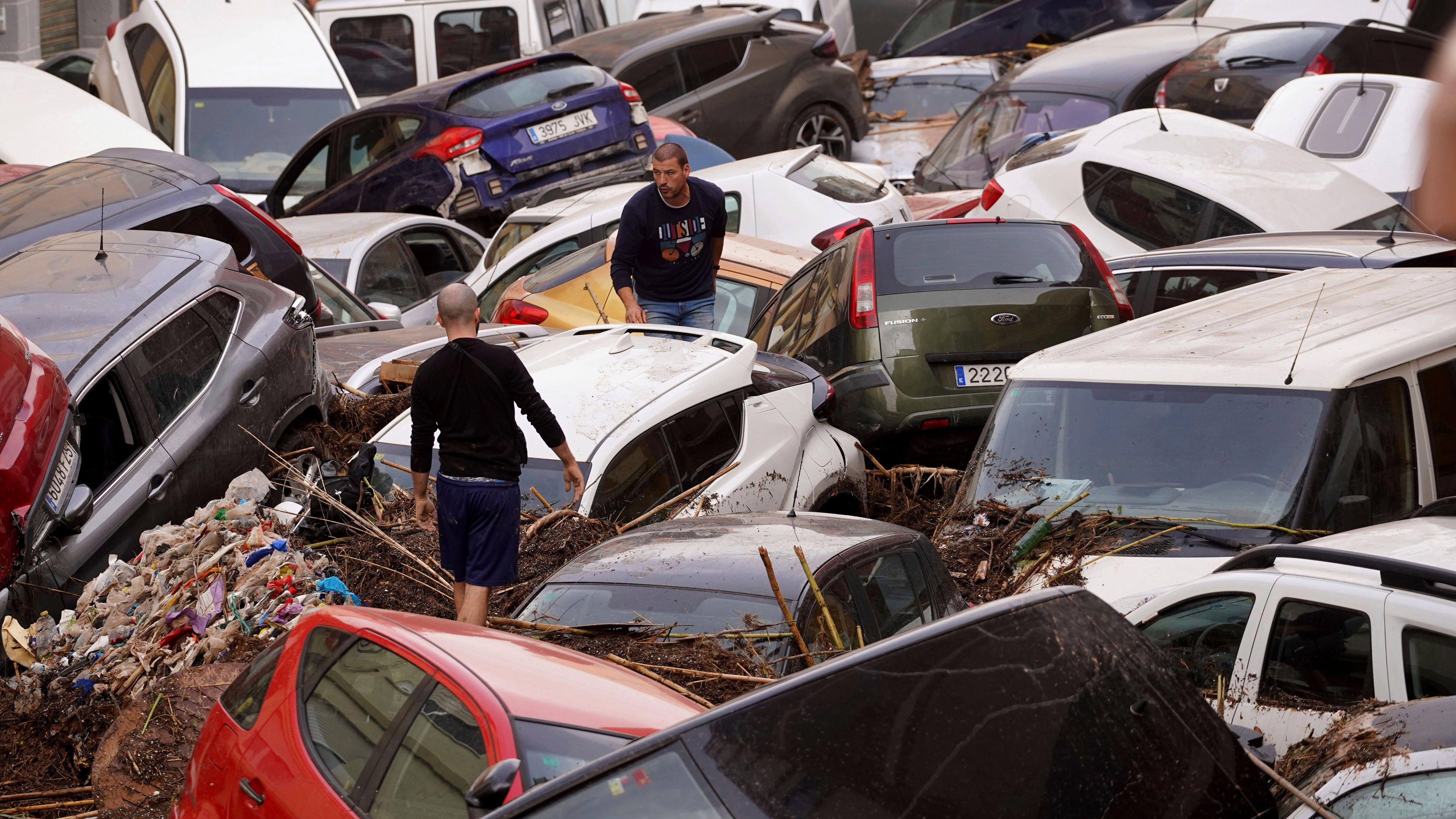 Anwohner betrachten durch die Wassermassen aufgestapelte Autos. 