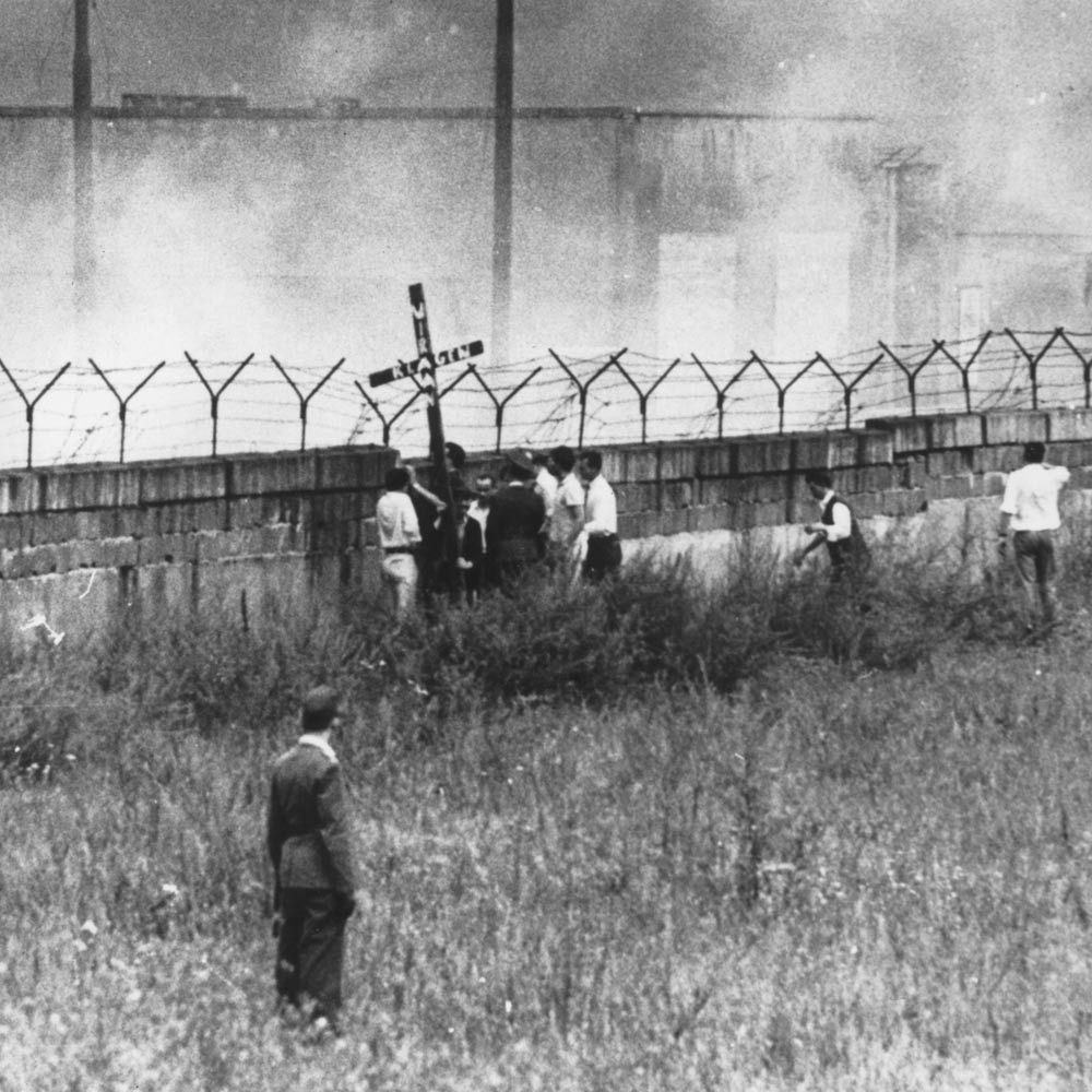 13. August 1962: Am 1. Jahrestag der Mauer hielten mehrere West-Berliner ein Holzkreuz in die Höhe. Darauf zu lesen: "Wir klagen an". 