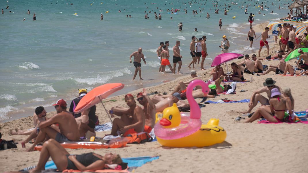 Menschen sonnen sich, genießen das Wetter und schwimmen am Strand von Arenal auf Mallorca.