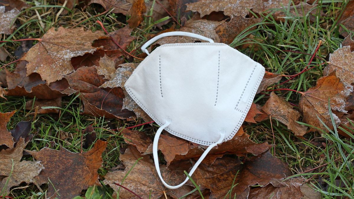 A used but clean medical respirator lies on the ground in the grass and autumn leaves in the hoarfrost. Late fall, early winter, frost.