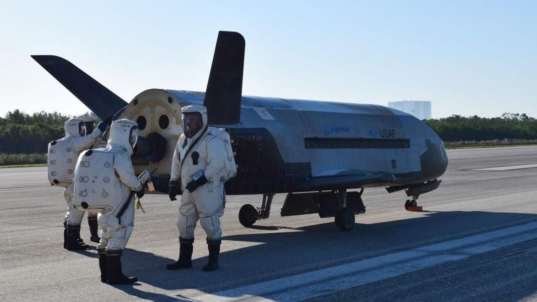 Das X-37B Orbital Test Vehicle im Mai 2017 am Kennedy Space Center in Florida. Die Anzüge schützen die Techniker vor giftigem Treibstoff.&nbsp;