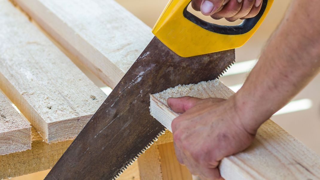 Handwerker bearbeitet Holzbretter mit einer Säge.