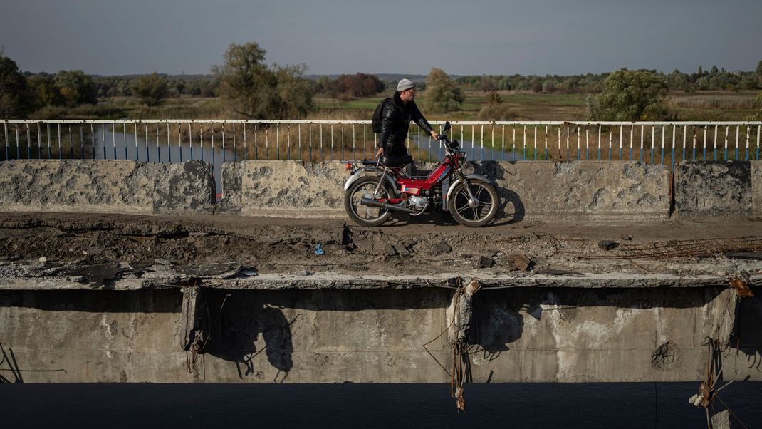Ein Mann zieht sein Motorrad auf einer zerstörten Brücke über den Fluss Oskil während einer Evakuierung in Kupjansk.