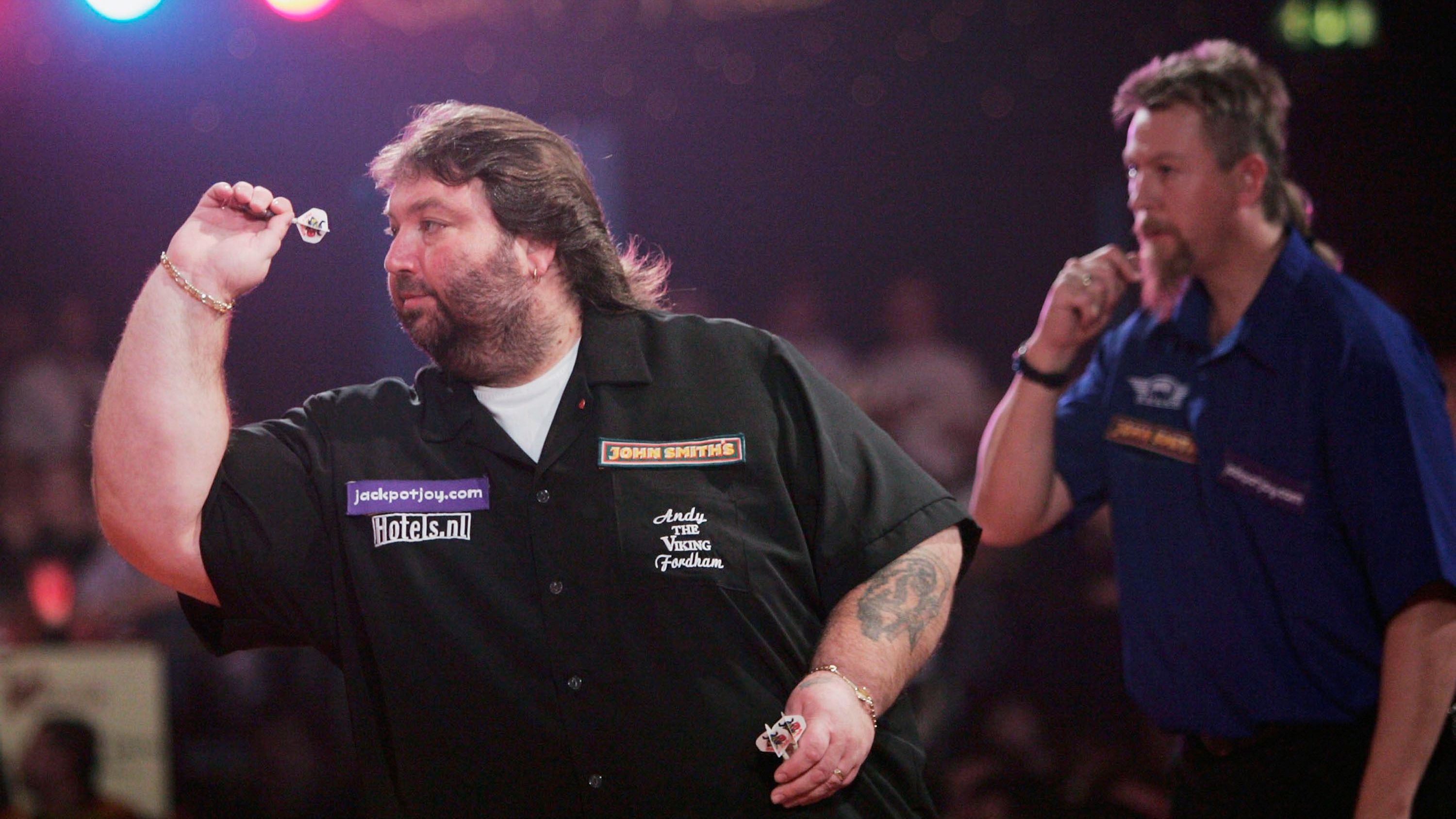 <strong>WM 2004: Andy Fordham (li.)</strong><br>2004 wurde Fordham BDO-Weltmeister. Zeit seines Wirkens hatte er mit einem Alkoholproblem zu kämpfen, wie er später offen zugab. Laut eigener Aussage trank er vor Matches auch mal 24 Bier und dazu noch Schnaps, so auch bei seinem WM-Sieg. 2007 kollabierte er hinter der Bühne, stellte anschließend sein Leben um, wurde trocken und nahm ab. 2021 verstarb er, auch infolge seines Lebensstils.