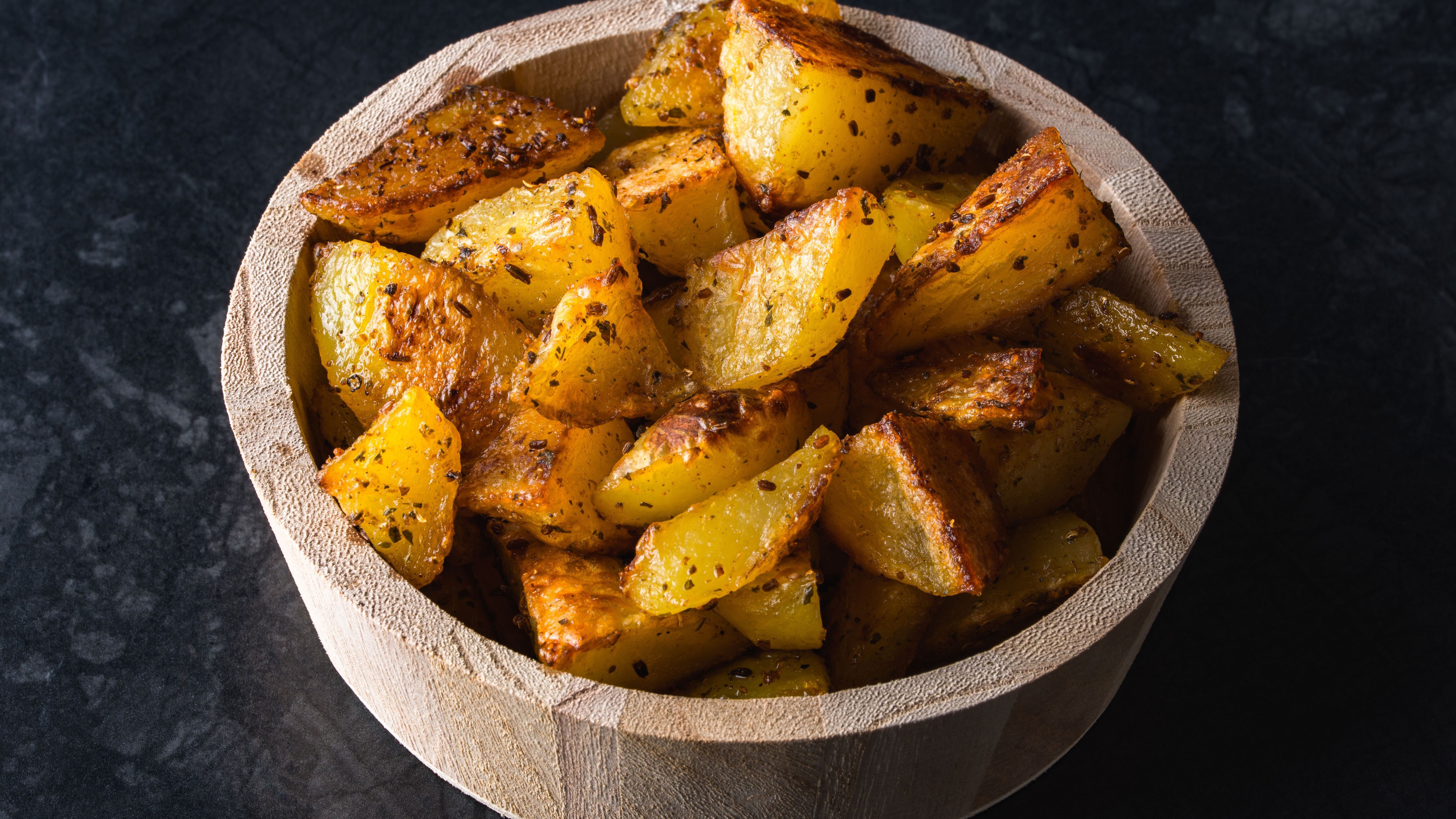 Grilled potatoes in wooden bowl on black background