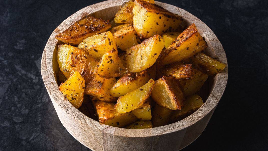 Grilled potatoes in wooden bowl on black background