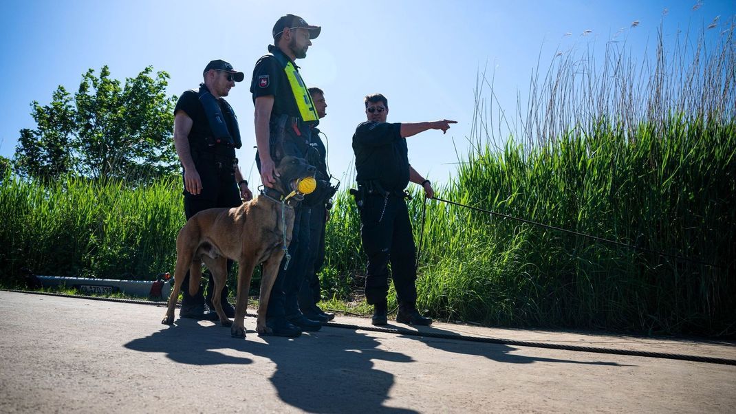Einsatzkräfte der Polizei stehen bei der Suche nach dem vermissten Arian mit einem Spürhund an der Oste.