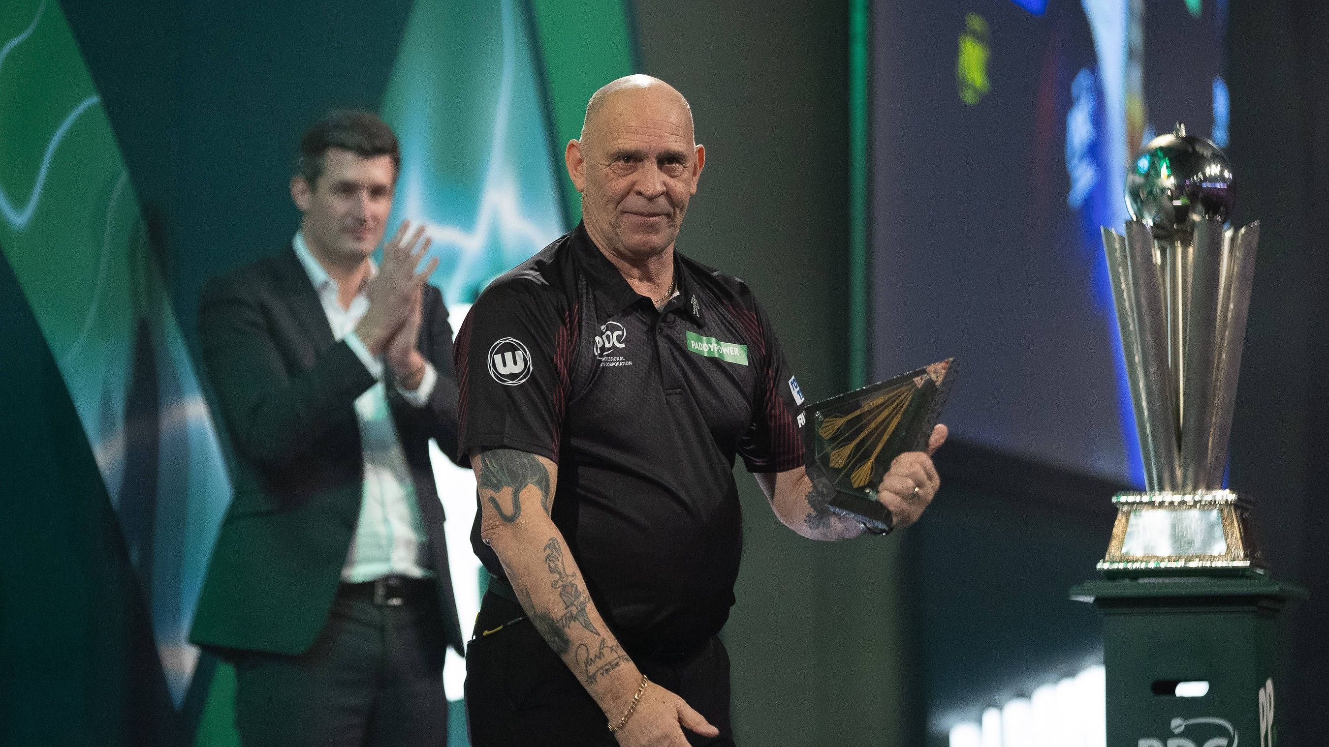 <strong>PDC Hall of Fame: Russ Bray</strong><br>Russ Bray war bei der kürzlich zuende gegangenen Darts-WM 2024 letztmals bei einem im Fernsehen übertragenen Match als Caller tätig. Er nahm an 28 Weltmeisterschaften teil. Die PDC Hat ihn nun in ihre Hall of Fame aufgenommen. <strong><em>ran</em></strong> zeigt, mit welchen Legenden sich Bray den Platz an der Sonne teilt.