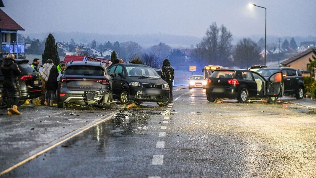 Nach einem Unfall bei Glatteis bei Aalen mit mehreren Fahrzeugen stehen Helfer und Beteiligte an den Autos auf einer Straße. 