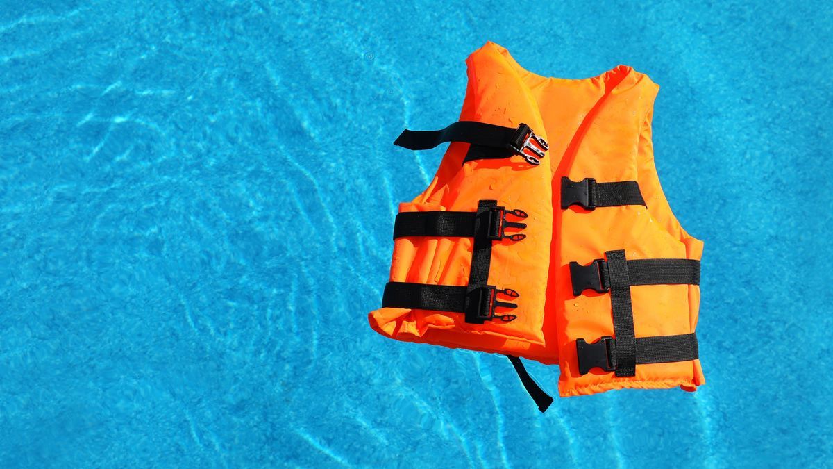 Bright orange life jacket floating in swimming pool, top view