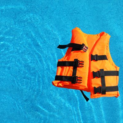 Bright orange life jacket floating in swimming pool, top view