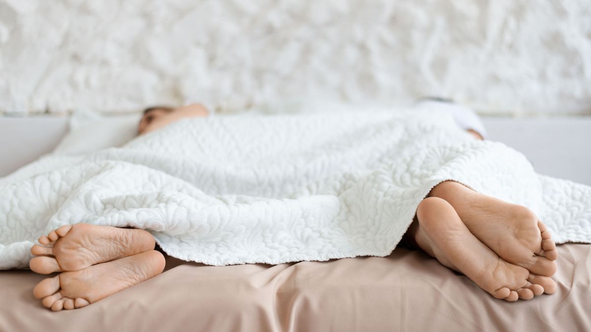 Sexual problems. Husband and wife lying apart with their backs to each other in bed, closeup of feet, free space