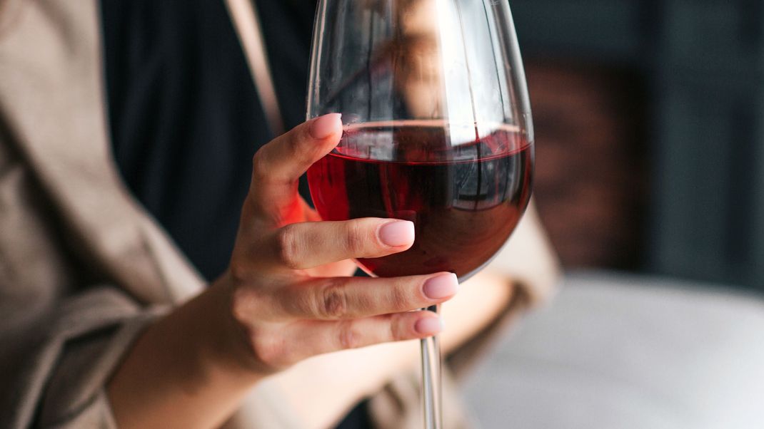 Cut view of woman's hand holding glass of red wine. Model wear black dress and brown shawl. Woman in living room alone.