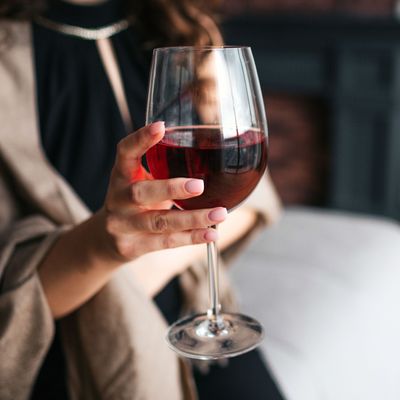 Cut view of woman's hand holding glass of red wine. Model wear black dress and brown shawl. Woman in living room alone.