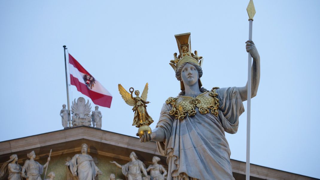 Ein Blick auf die Statue der griechischen Göttin der Weisheit, Pallas Athene, vor einer österreichischen Flagge auf dem österreichischen Parlament.