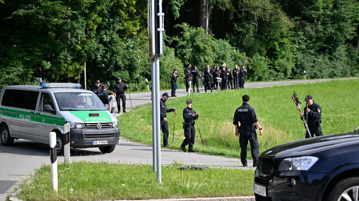 Polizeikräfte suchen eine Wiese und den Wald nach Beweismitteln in einem Mordfall ab. 