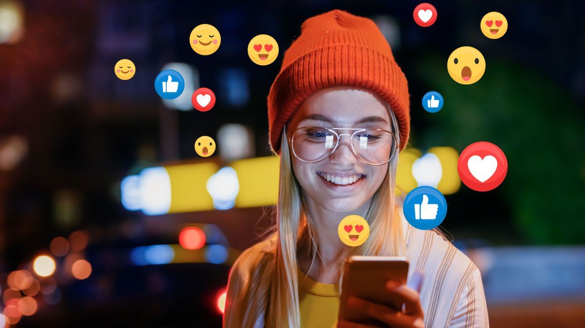A beautiful young woman blogger, vlogger or influencer is receiving emoji and emoticon reactions in her mobile smart phone device while making a post, sharing or video logging on social media