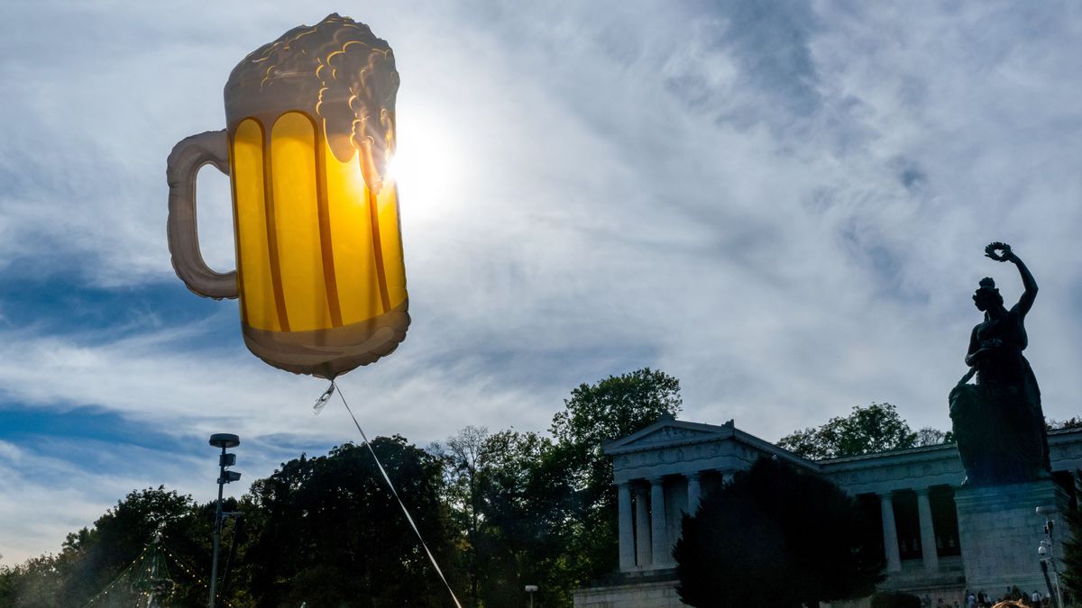 Ein Luftballon in Form eins Bierkruges schwebt auf dem Oktoberfestgelände vor der Kulisse der Bavaria.