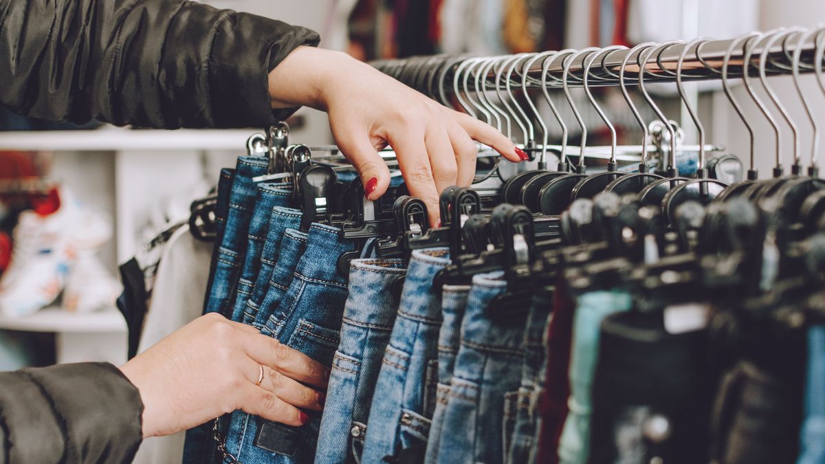 Fast fashion concept. Woman chooses jeans in a store. Lots of clothes in the store. Fast Fashion Destroying Planet.