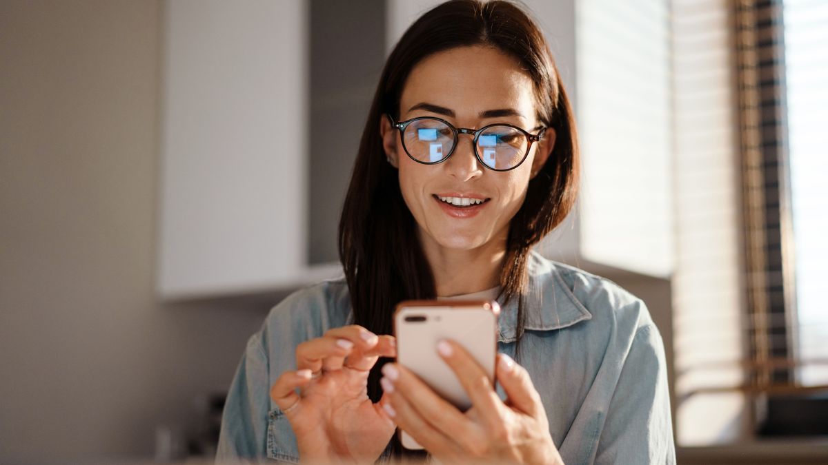 Glückliche Frau benutzt ihr Handy, während sie vor ihrem Laptop sitzt