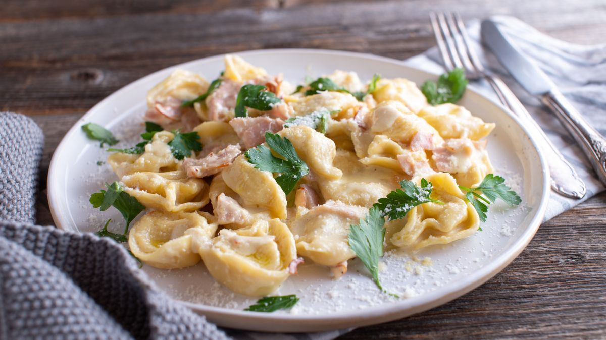 Plate with italian pasta dish. Tortellini with ham, parmesan cheese and parsley in a delicious cream sauce