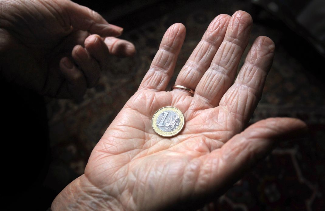 Eine 83-jährige Frau hält eine Euromünze in der Hand.