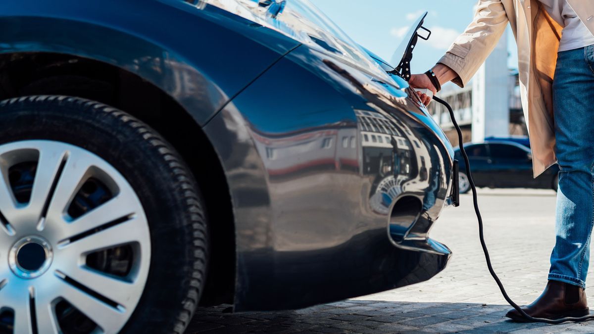 Stylish man in sunglasses disconnects the charging cable from his electric car