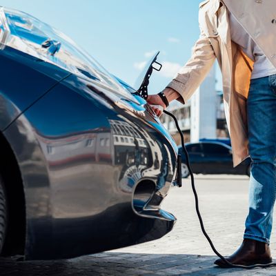 Stylish man in sunglasses disconnects the charging cable from his electric car