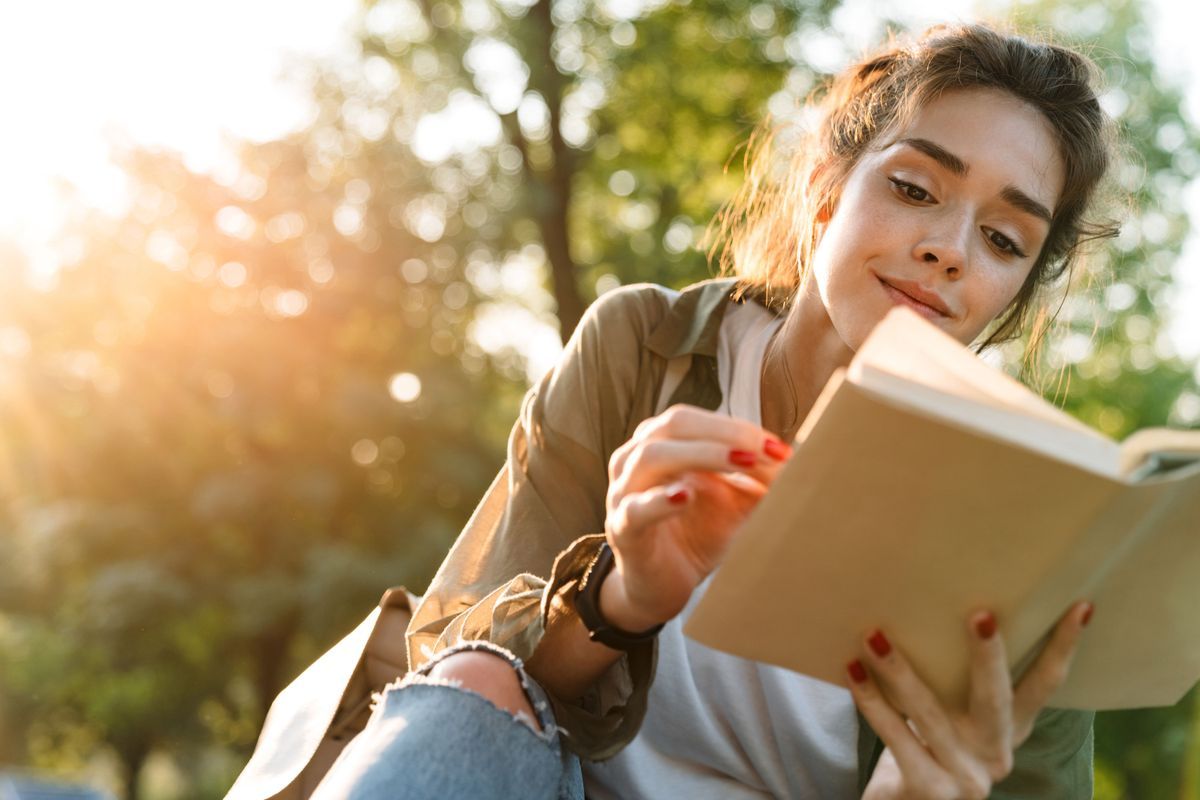 Image of young woman smiling and reading book in green park